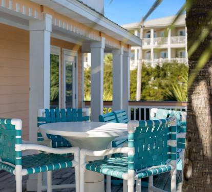 Enjoy morning coffee at your private table surrounded by turquoise chairs, swaying palms, and coastal charm on this peaceful covered porch.