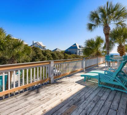 Spacious deck with turquoise lounge chairs overlooks coastal homes and palm trees under clear blue skies.