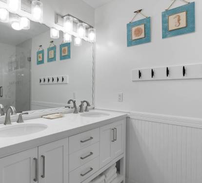 Step into your coastal-themed bathroom featuring dual vanities, elegant lighting, and beachy artwork that creates a spa-like retreat.
