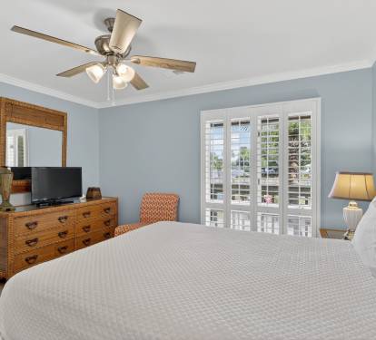 Relax in your serene bedroom featuring soothing blue walls, a comfortable bed with crisp linens, and French doors opening to your private balcony with outdoor views.