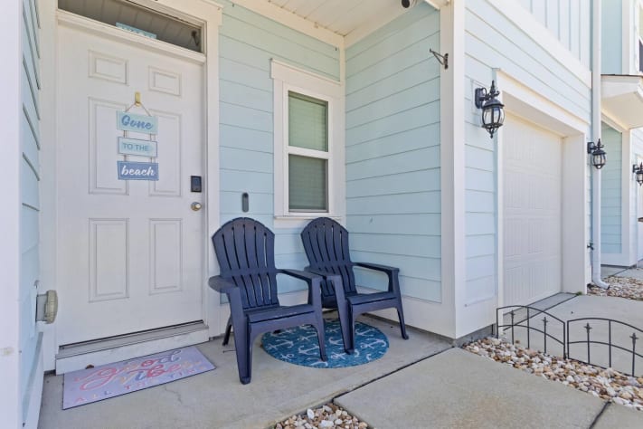 Charming front entry with coastal d&eacute;cor and a cozy seating area. Enjoy a welcoming porch with two chairs perfect for morning coffee or relaxing before heading out to explore the beach and nearby attractions.