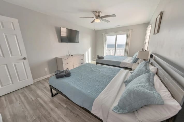 Bright bedroom with two full beds, dresser, and mounted TV.