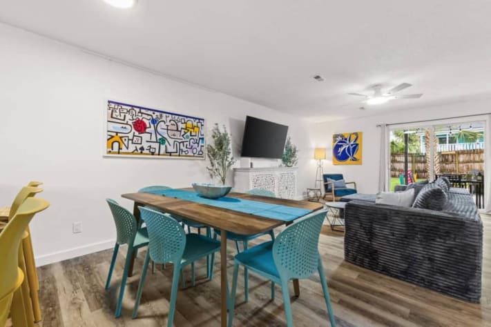 Gather at Unit B's dining table for six, with three more seats at the kitchen island. The open layout keeps cooks and guests connected to the oversized sectional and smart TV, while sliding doors lead to the covered patio and fenced backyard