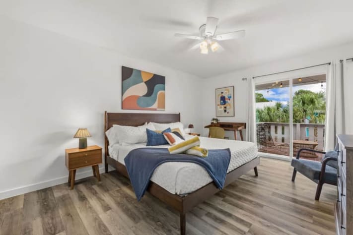 Unit B's upstairs primary suite offers a king bed for two, smart TV, dedicated desk, closet storage, and access to its own covered balcony. The private ensuite has a walk-in shower and a toilet with a bidet. Bed linens and towels are provided