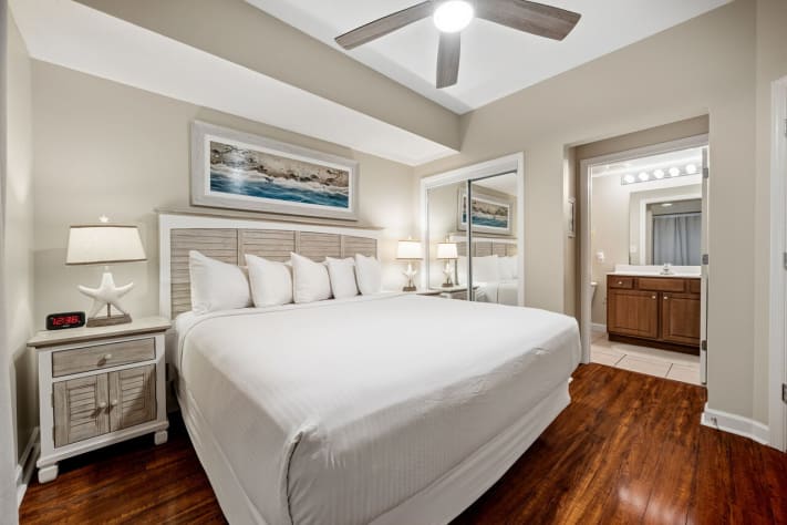 Bright coastal king bedroom with ensuite bath and ceiling fan