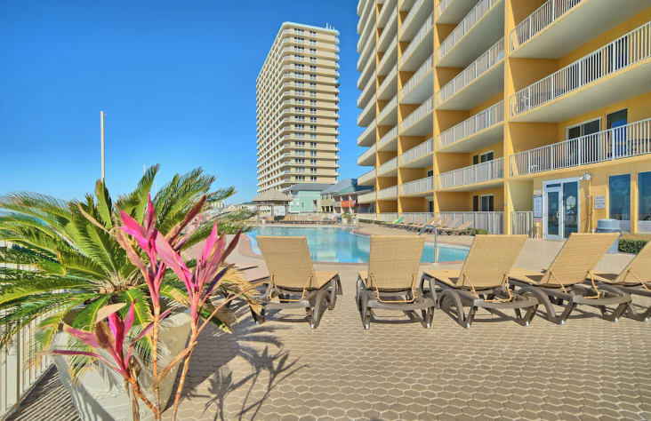 A hotel pool area with lounge chairs and a large building in the background.