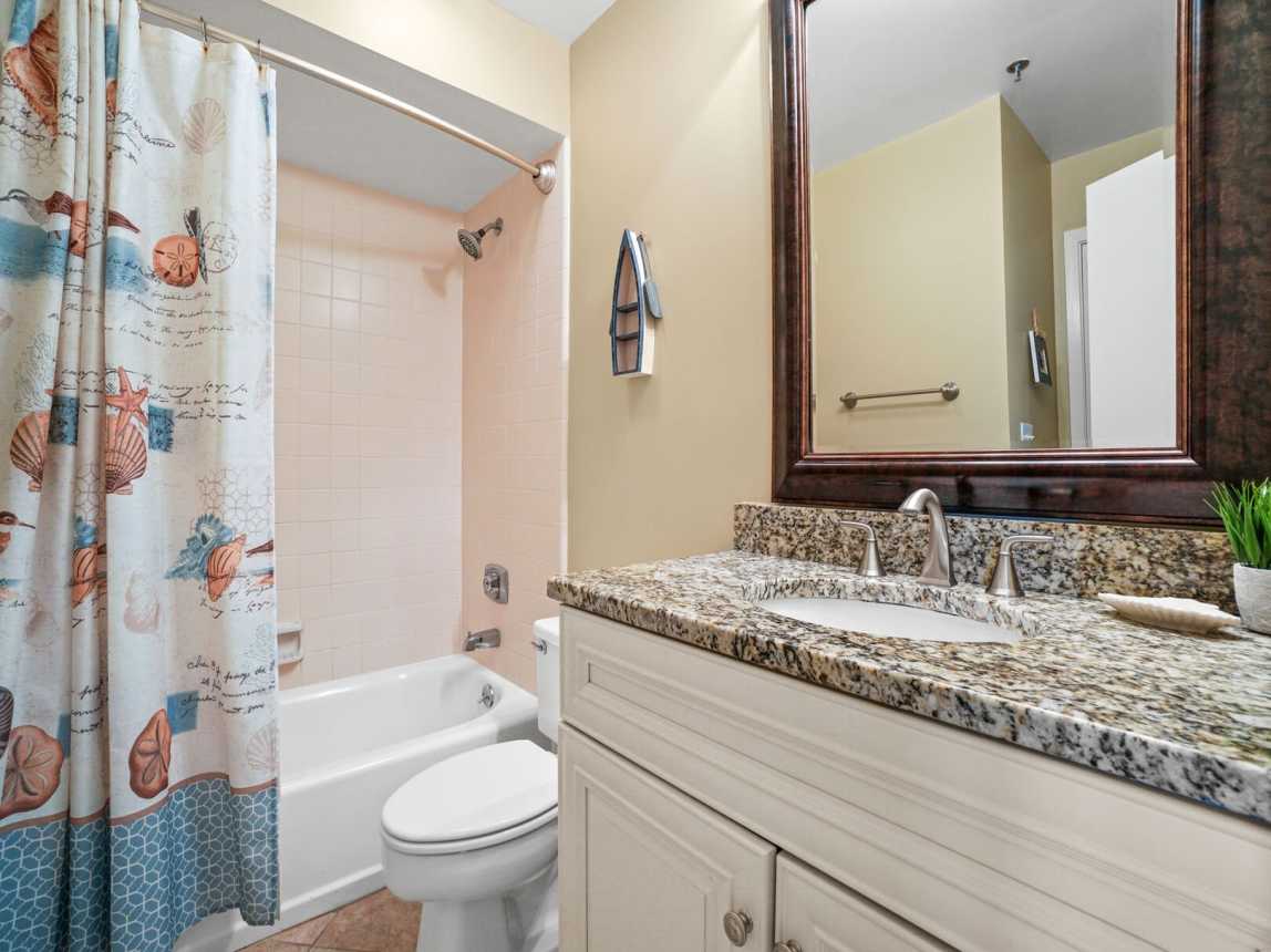 Guest bath has granite counters, mirror, single sink, under cabinet storage and a tub/shower combo.