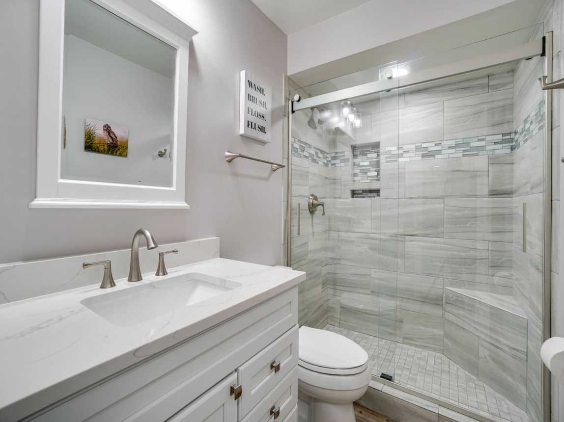 Just outside your bedroom is a bath with a step in tiled shower with seat and a 1 sink vanity and mirror.