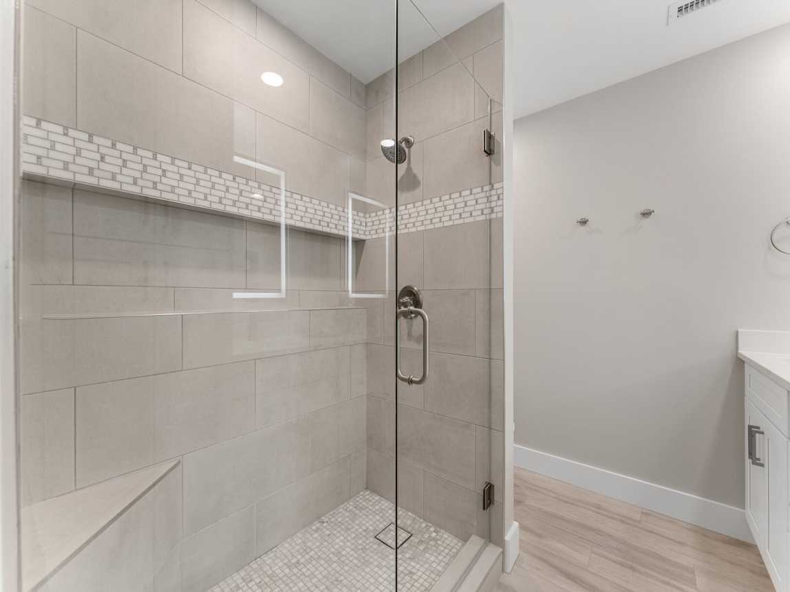 Oversize tiled step in shower has a rain shower head and shower seat and shower ledge for bath accessories.