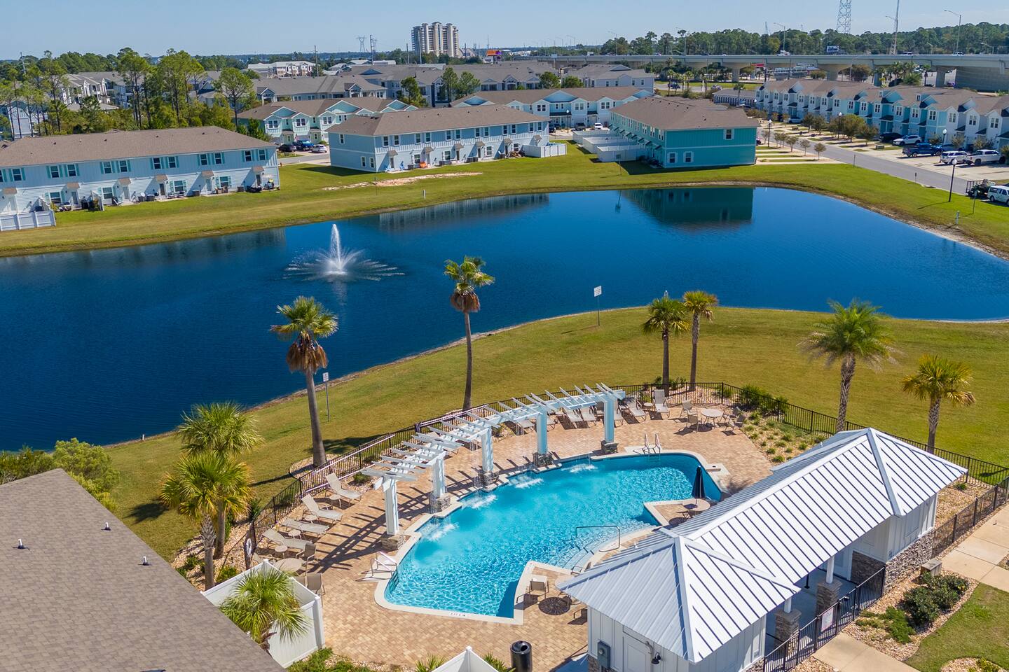 Beautiful resort-style community pool surrounded by palm trees, lounge chairs, and shaded seating. A perfect spot to swim, relax, and enjoy the sunny coastal atmosphere during your stay.