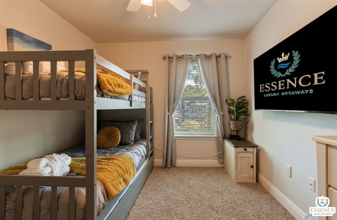 Fun and cozy bunk bedroom perfect for kids or groups, featuring comfortable beds, soft linens, and a wall-mounted TV. Bright natural light and thoughtful d&eacute;cor make this space ideal for relaxing after a day of adventure.