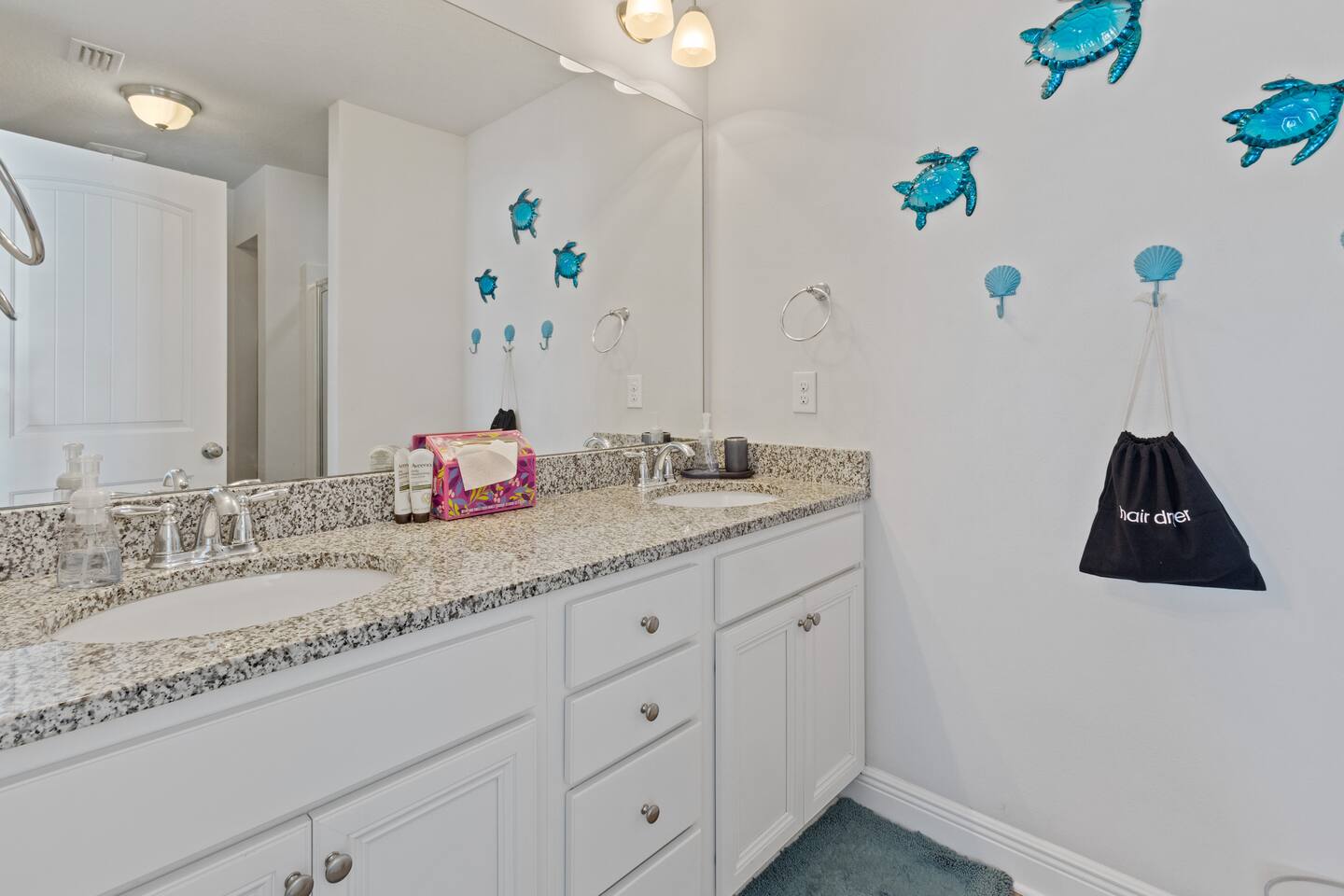 Bright, clean bathroom with a spacious double vanity, granite countertops, and large mirror. Coastal-inspired d&eacute;cor adds a fun touch, with plenty of space for guests to get ready comfortably.