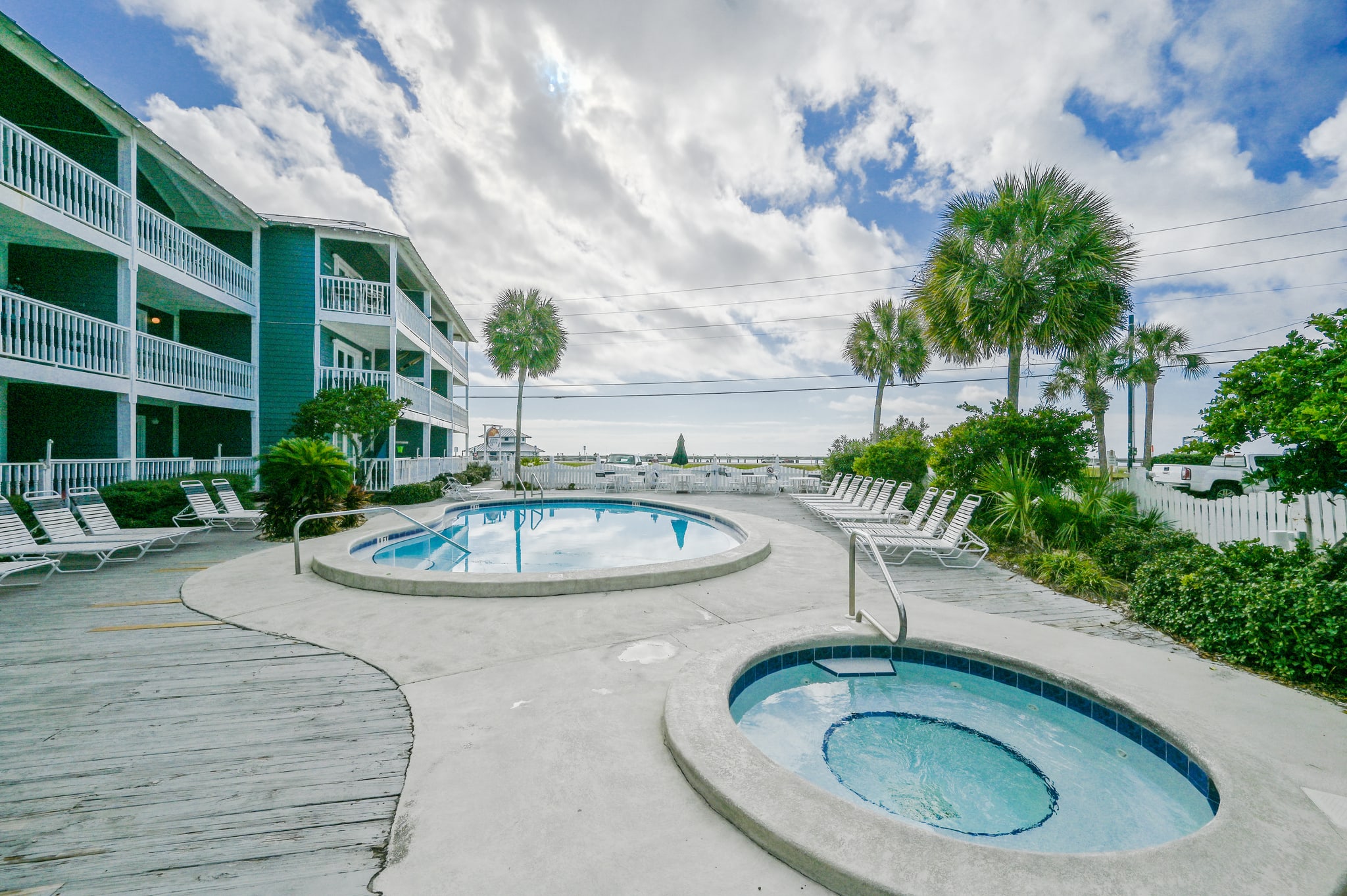 This picture shows the heated pool and hot tub located out the the patio gate of our beach condo. The pool is surrounded by a deck with lounge chairs, while the hot tub is tucked away in the corner. The crystal clear blue water sparkles in the sun, and th