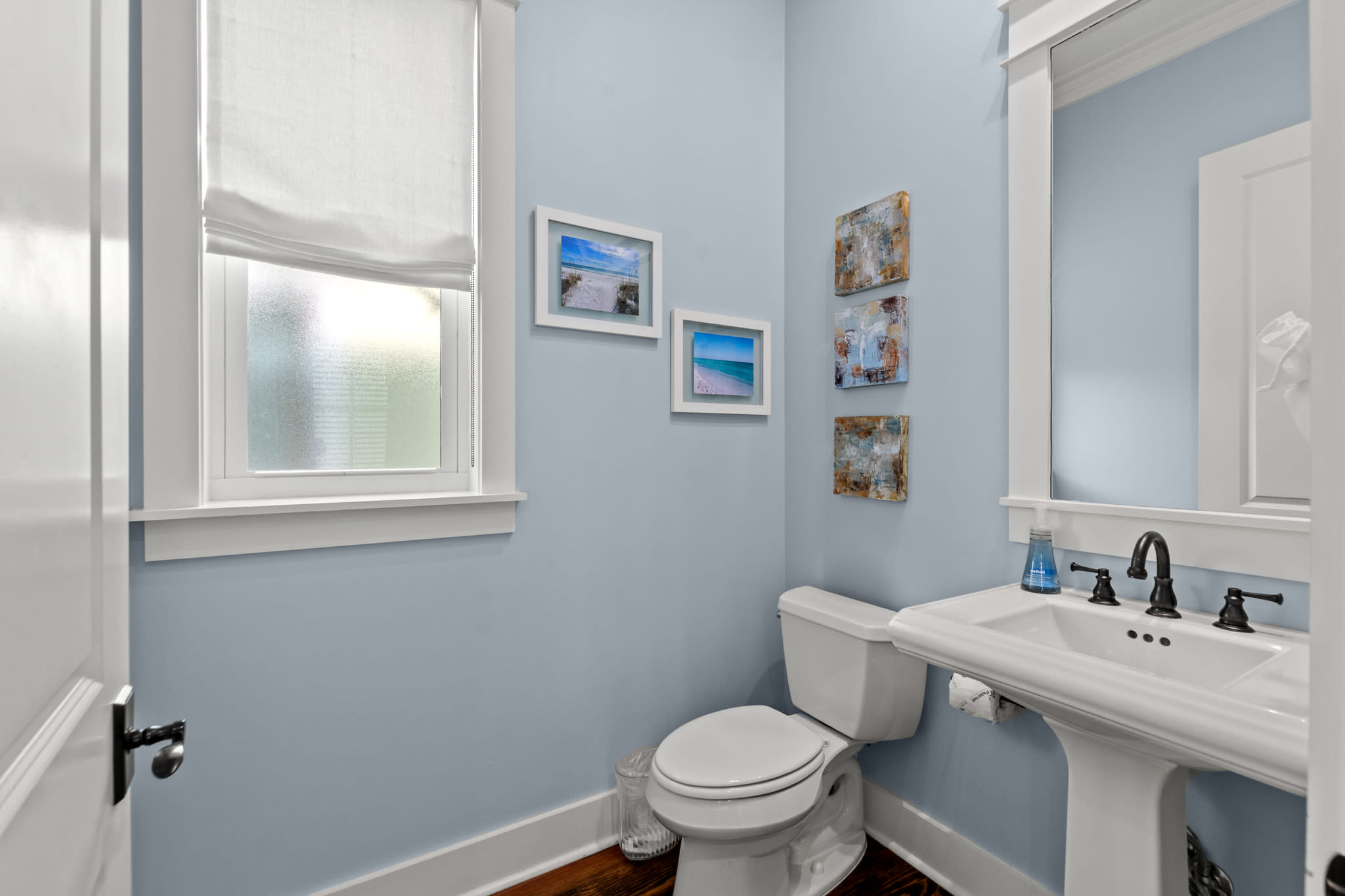 Clean half bath w/ pedestal sink, coastal art & soft blue walls for a fresh feel. Clean half bath w/ pedestal sink, coastal art & soft blue walls for a fresh feel.