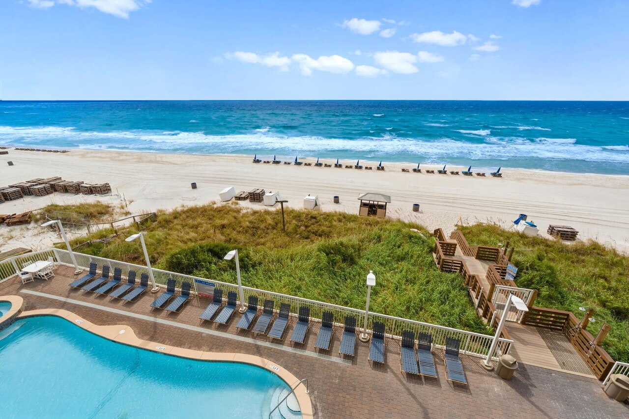Resort pool overlooking dune walkover, beach chairs, and Gulf waves