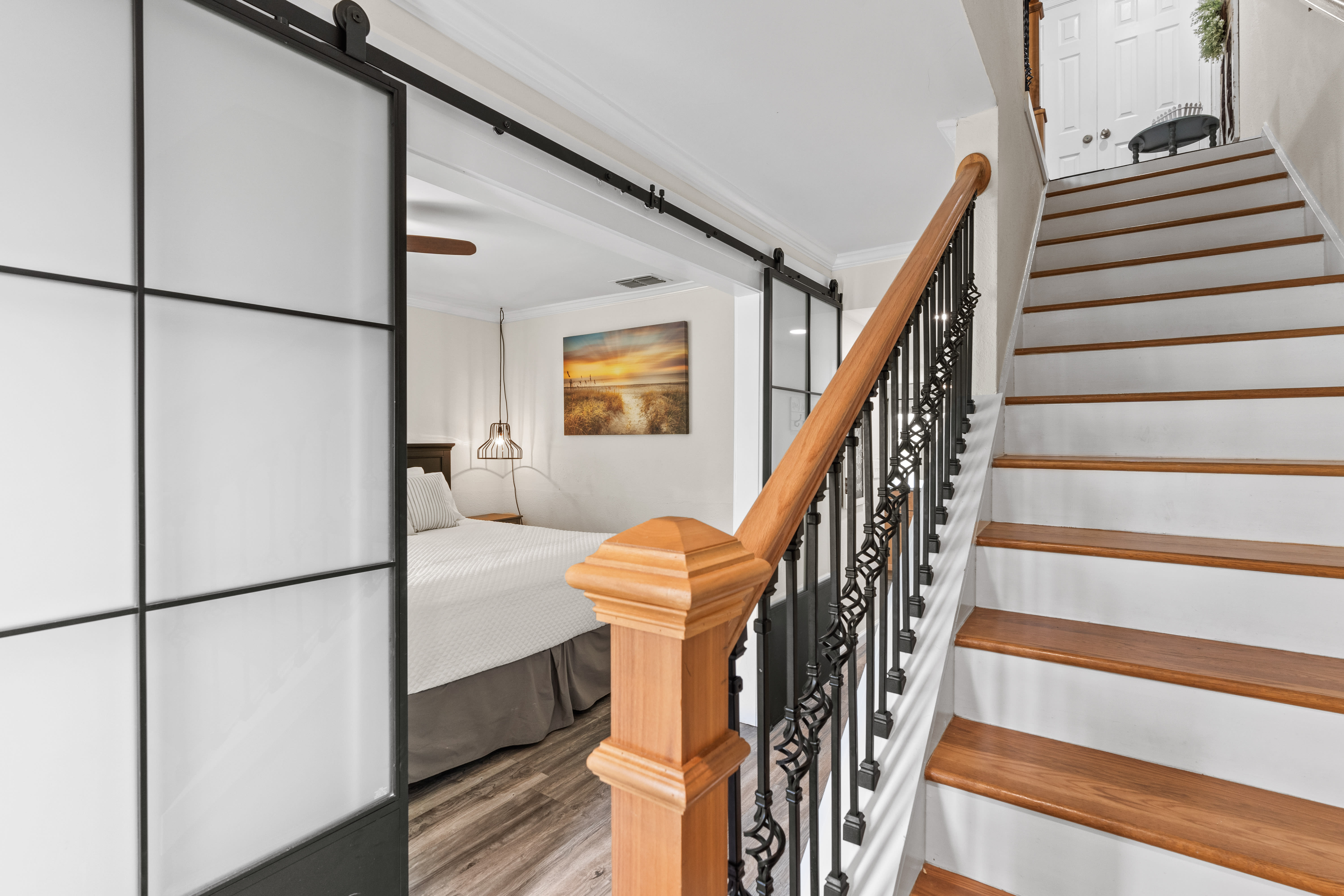 Elegant wooden stairs lead to your private bedroom loft, where modern barn doors create intimate separation while preserving the open, airy feel.