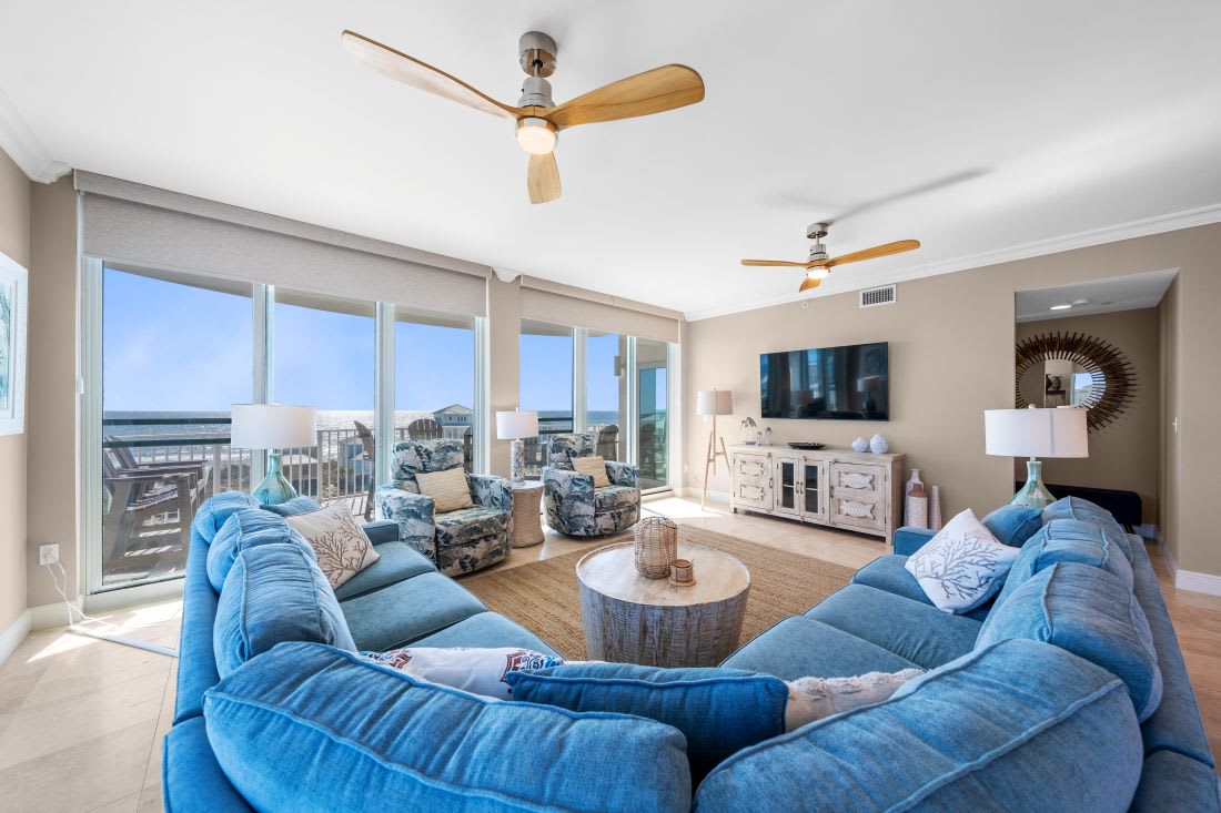 Unwind in your spacious living room where plush blue seating surrounds a rustic coffee table, while floor-to-ceiling windows frame stunning views.