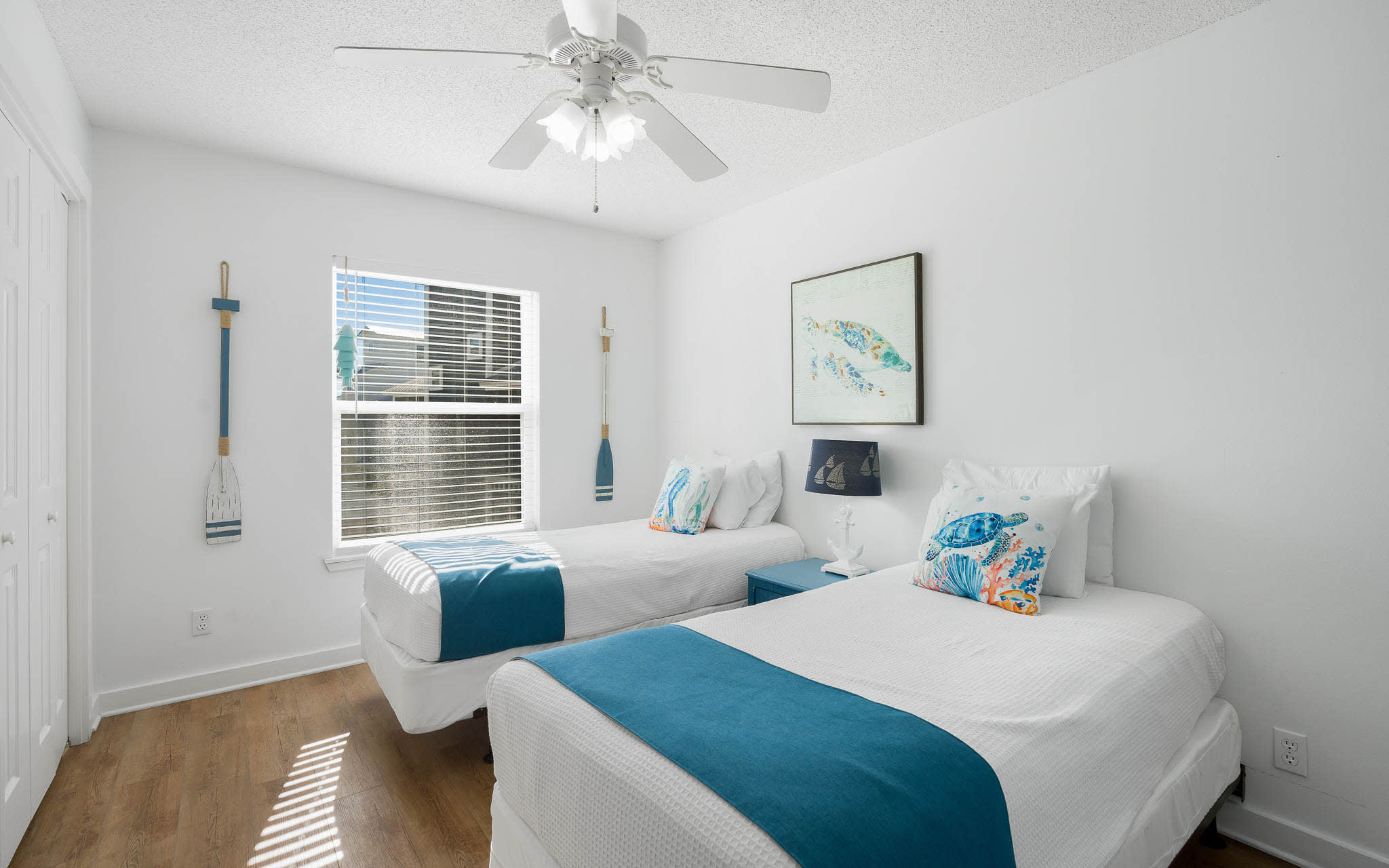 Drift off to sleep in this bright coastal bedroom with twin beds, nautical touches, and gentle ceiling fan breeze.