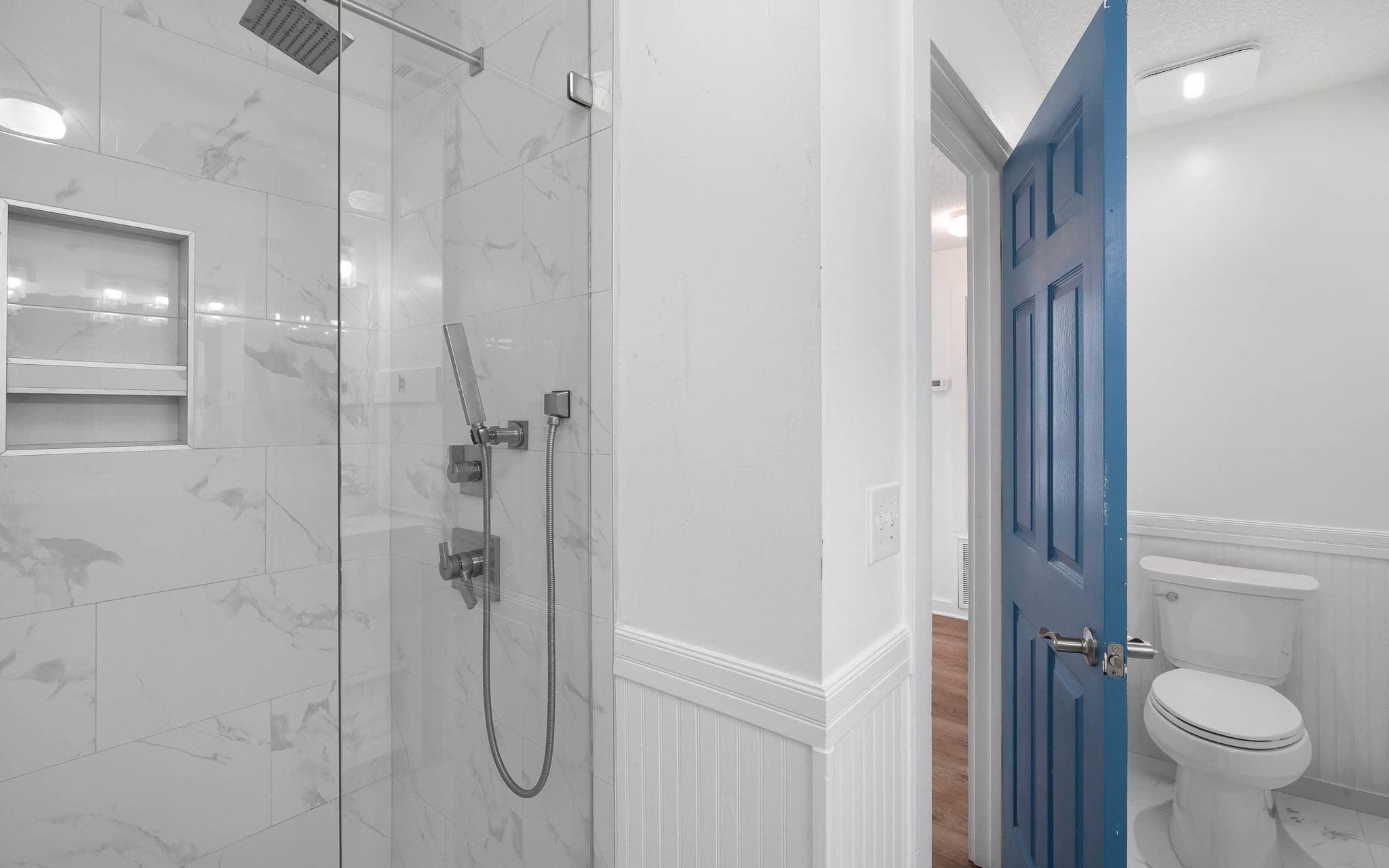 Step into your pristine marble bathroom featuring a luxurious rainfall shower and elegant blue door detail for a spa-like retreat.