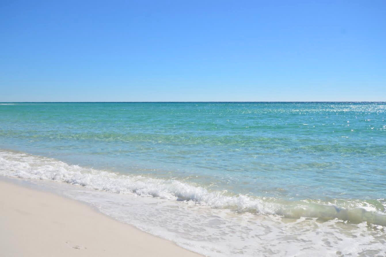 Clear emerald Gulf waters gently meeting sugar-white sand, creating a serene coastal shoreline perfect for swimming, beach walks, and soaking up the relaxed Emerald Coast atmosphere.