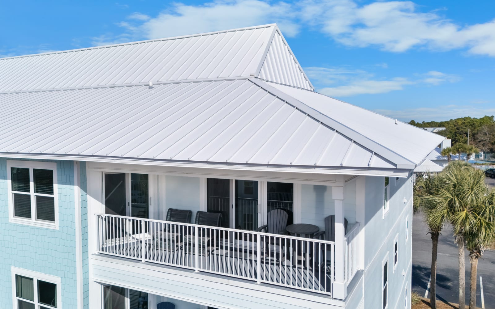 Modern coastal property featuring white metal roofing and covered balcony with scenic neighborhood views.