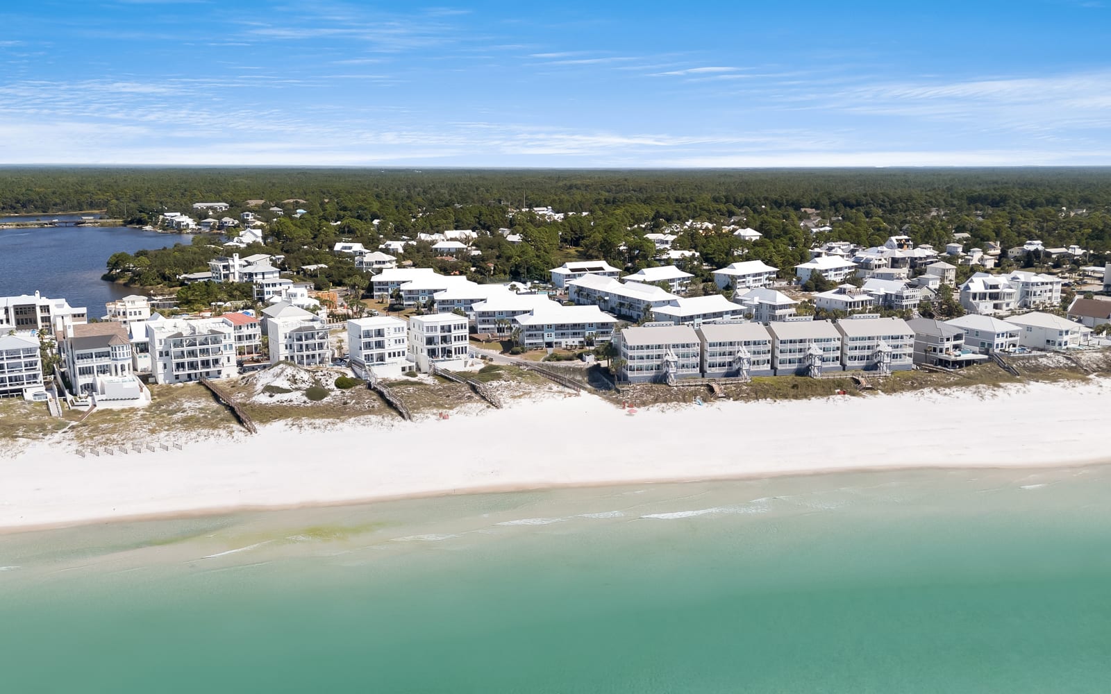 Aerial view of beachfront properties nestled along pristine white sand and emerald waters, surrounded by lush coastal forest.