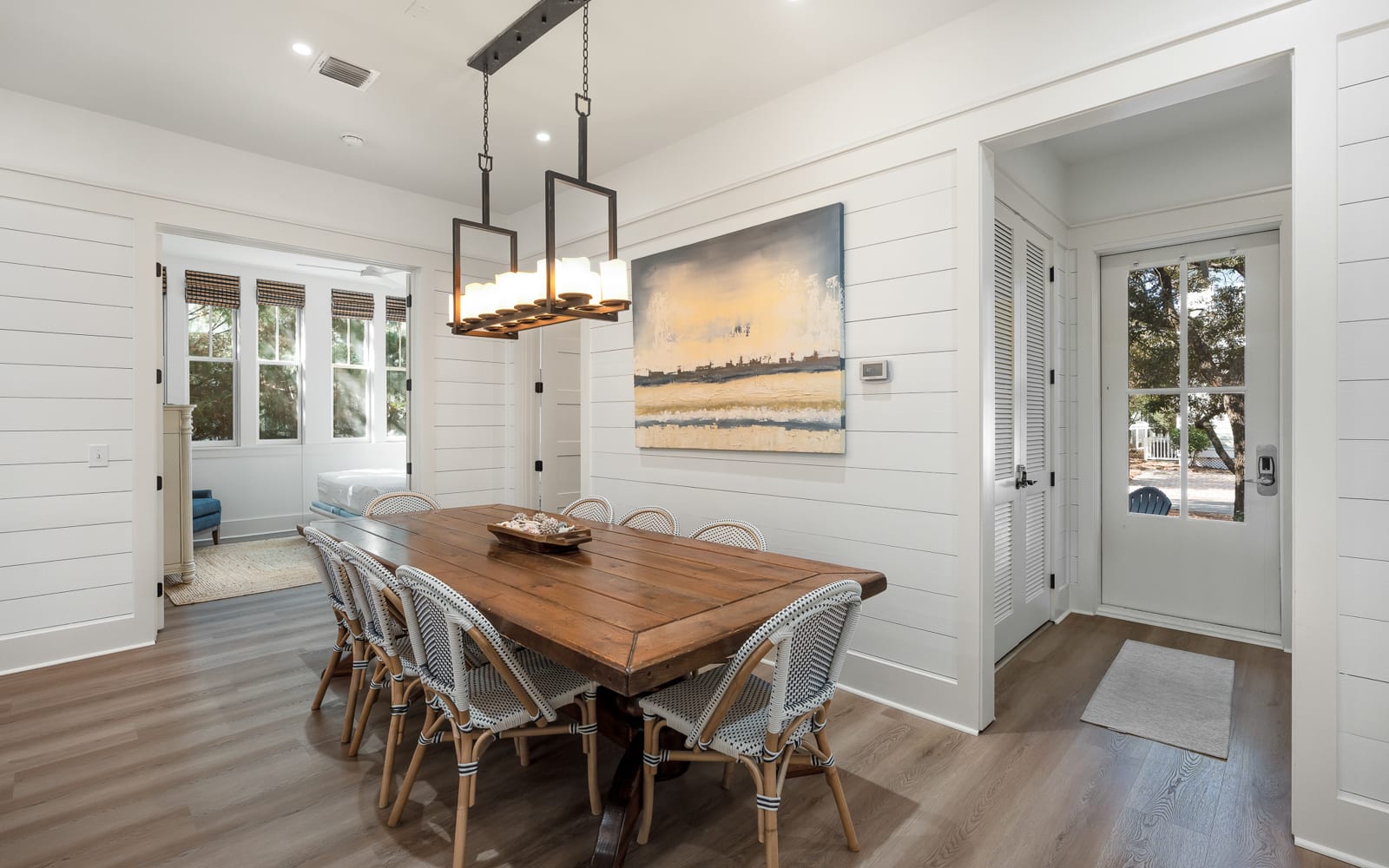 Gather around this stunning dining table where coastal artwork and warm lighting create the perfect setting for your memorable meals together.