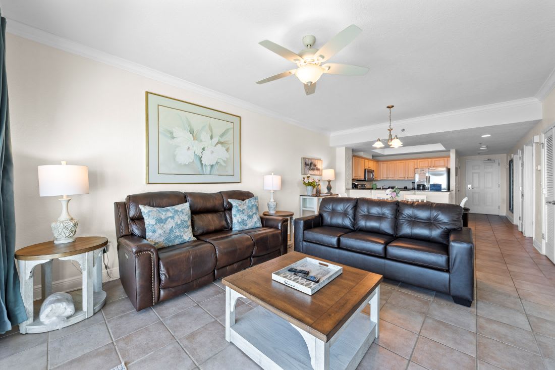 Relax in your spacious living room with comfortable leather seating, ceiling fan, and open concept design flowing into the full kitchen.