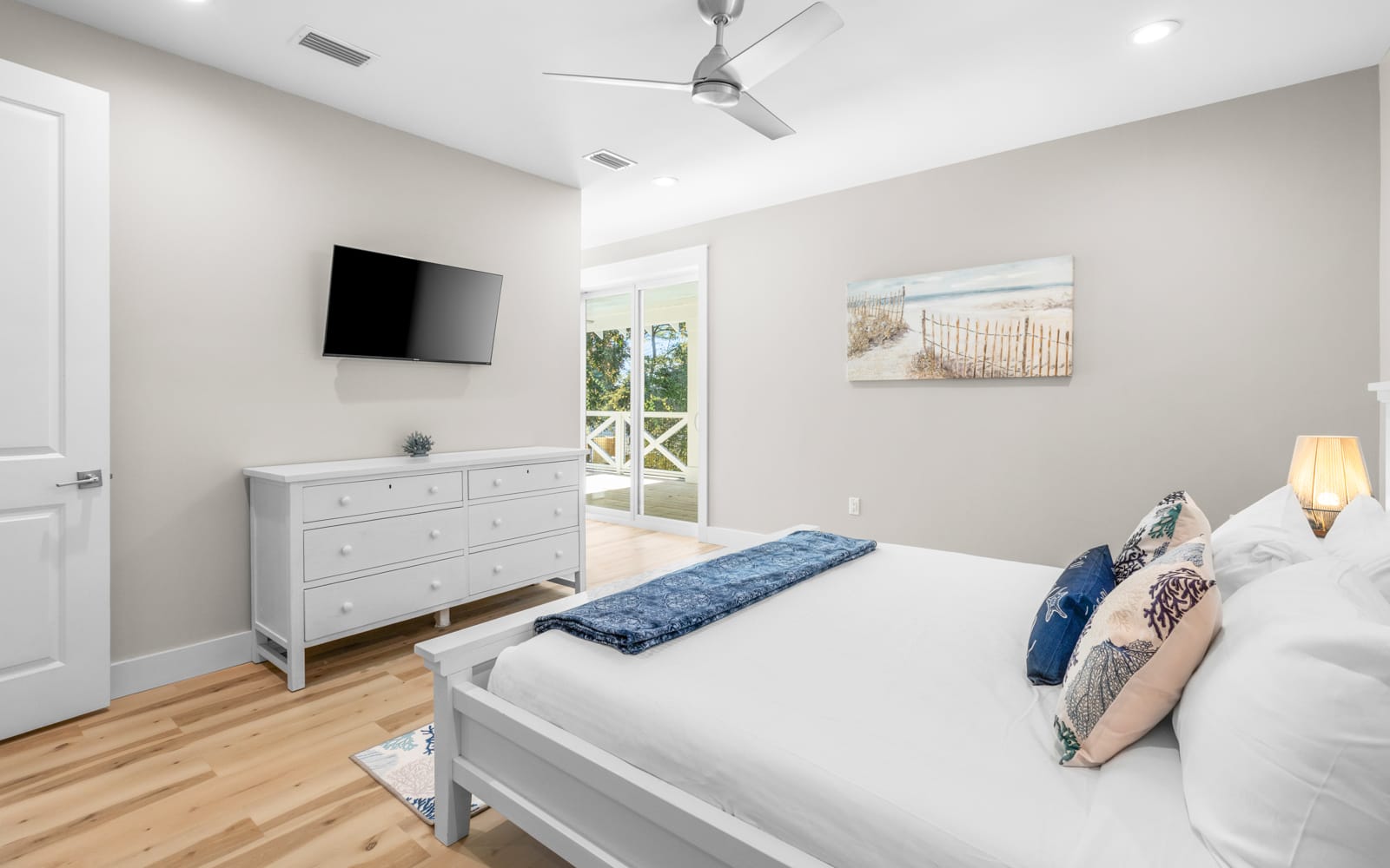 Drift off in this serene coastal bedroom with crisp linens, warm wood floors, and gentle ocean breezes from your private balcony.