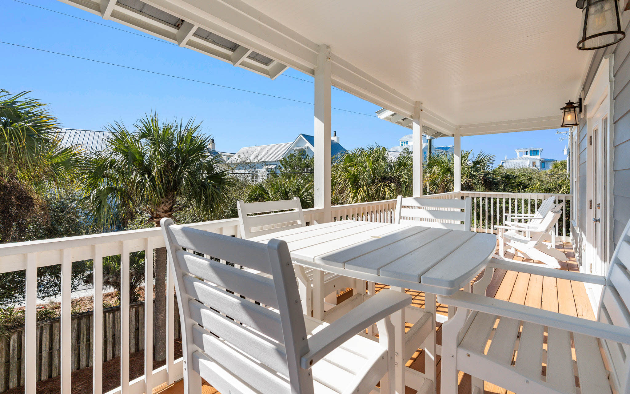 Step onto your private covered deck where white dining furniture awaits under swaying palm trees and coastal views.