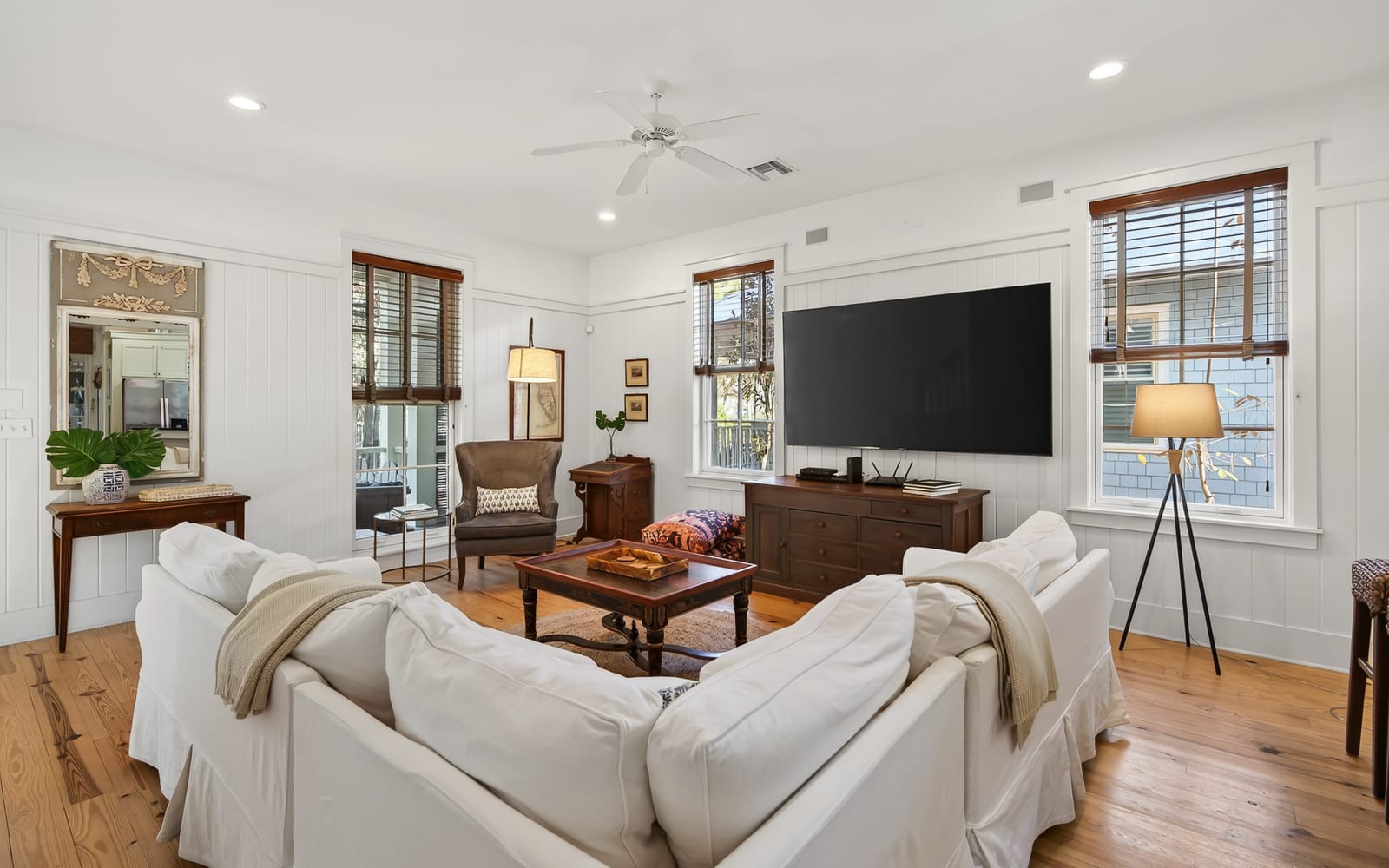 Unwind in this elegant living room with plush white sofas, warm hardwood floors, and modern entertainment setup for your perfect retreat.