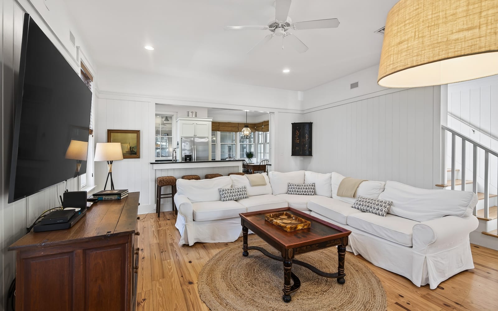 Sink into plush white sofas in your bright living room, where coastal charm meets modern comfort with soaring ceilings and open kitchen views.