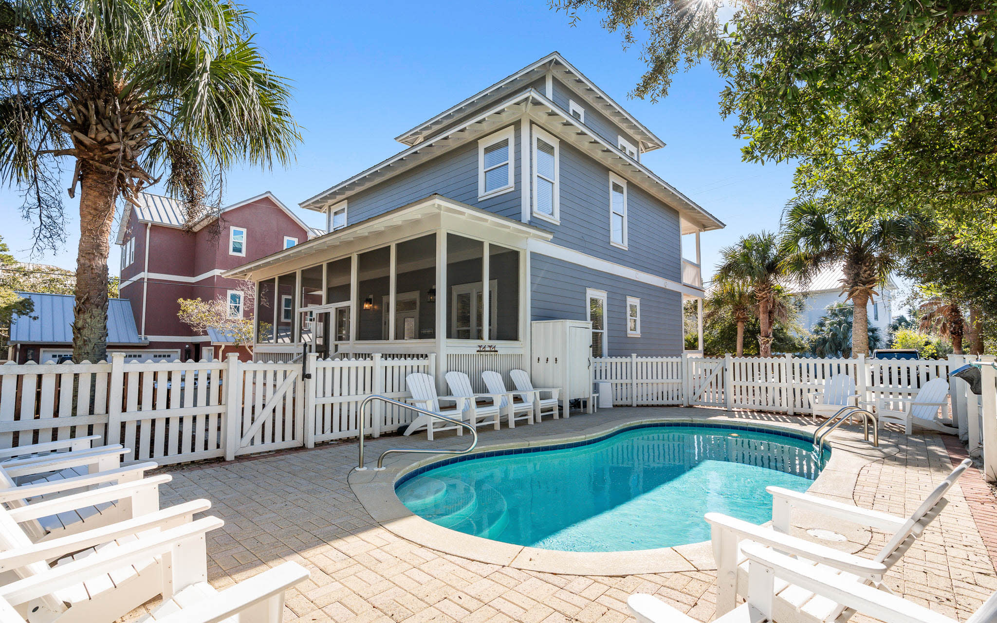 Charming coastal home with private pool surrounded by palm trees and white picket fence for your perfect beach getaway.