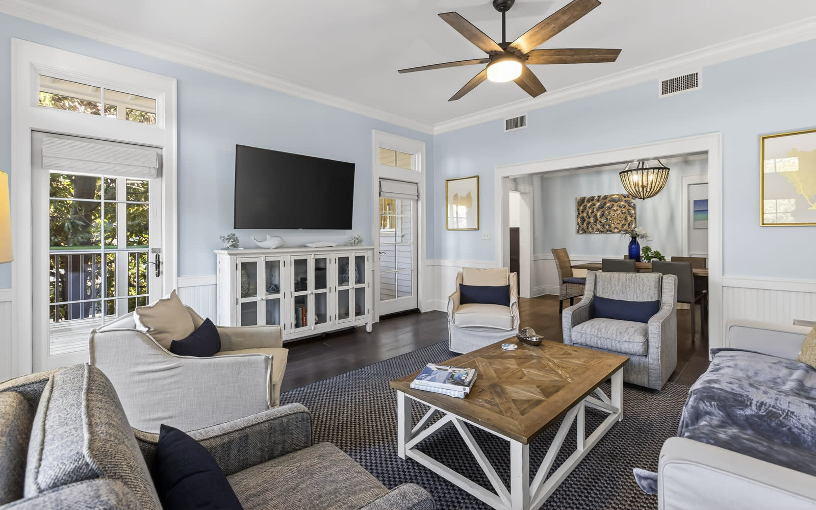 Relax in your stylish living room featuring cozy seating, a large TV, and gentle ceiling fan breeze flowing through French doors.