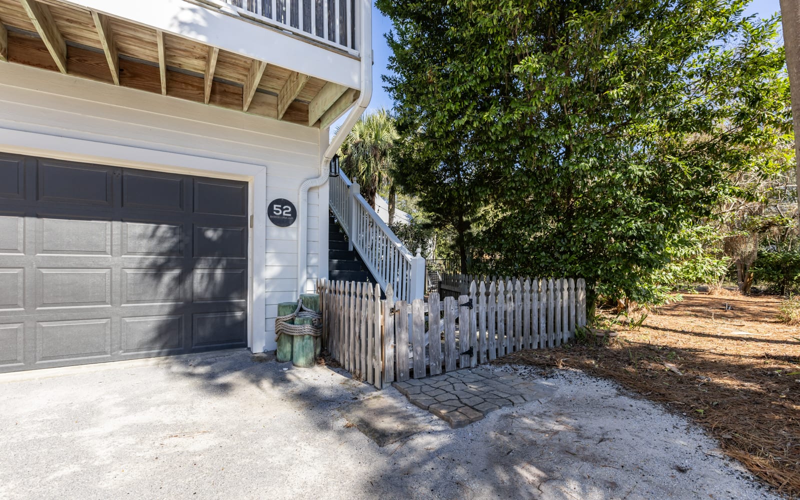 Charming coastal property entrance with convenient garage parking and natural landscaping in a peaceful residential setting.