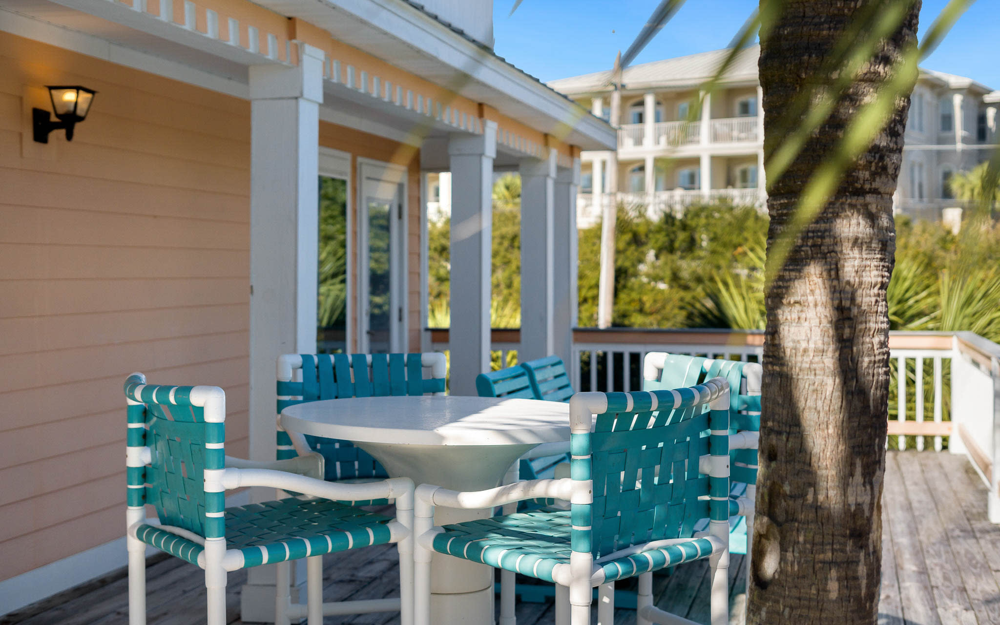 Enjoy morning coffee at your private table surrounded by turquoise chairs, swaying palms, and coastal charm on this peaceful covered porch.