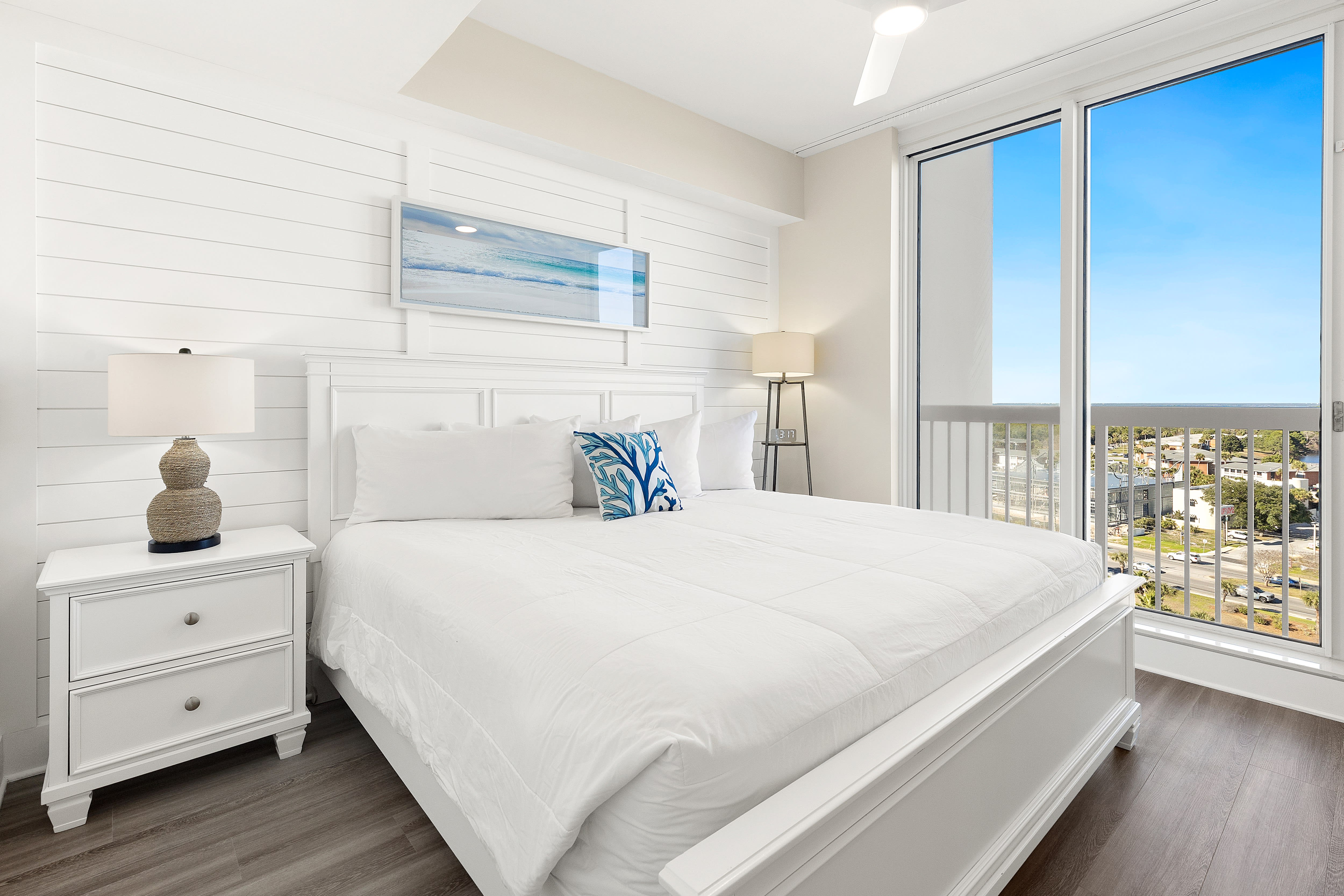 Drift into peaceful sleep in your bright coastal bedroom with crisp white linens and stunning city views through floor-to-ceiling windows.