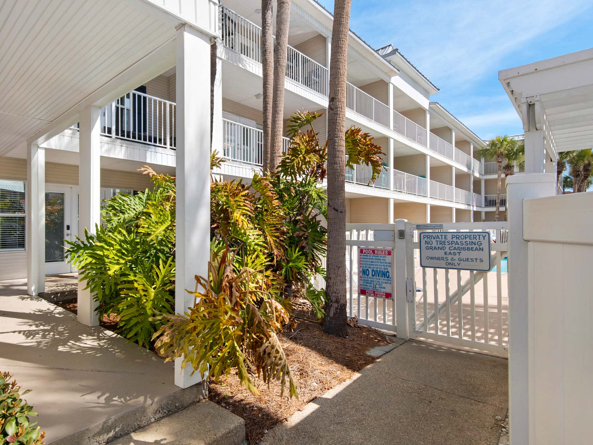 Tropical Caribbean-style property featuring white buildings with balconies surrounded by lush palm trees and colorful foliage.