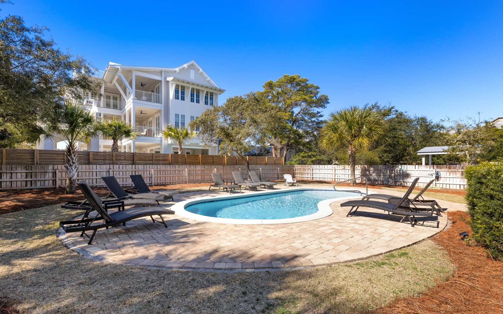 Private pool oasis with comfortable loungers surrounded by mature landscaping and stunning white coastal architecture.