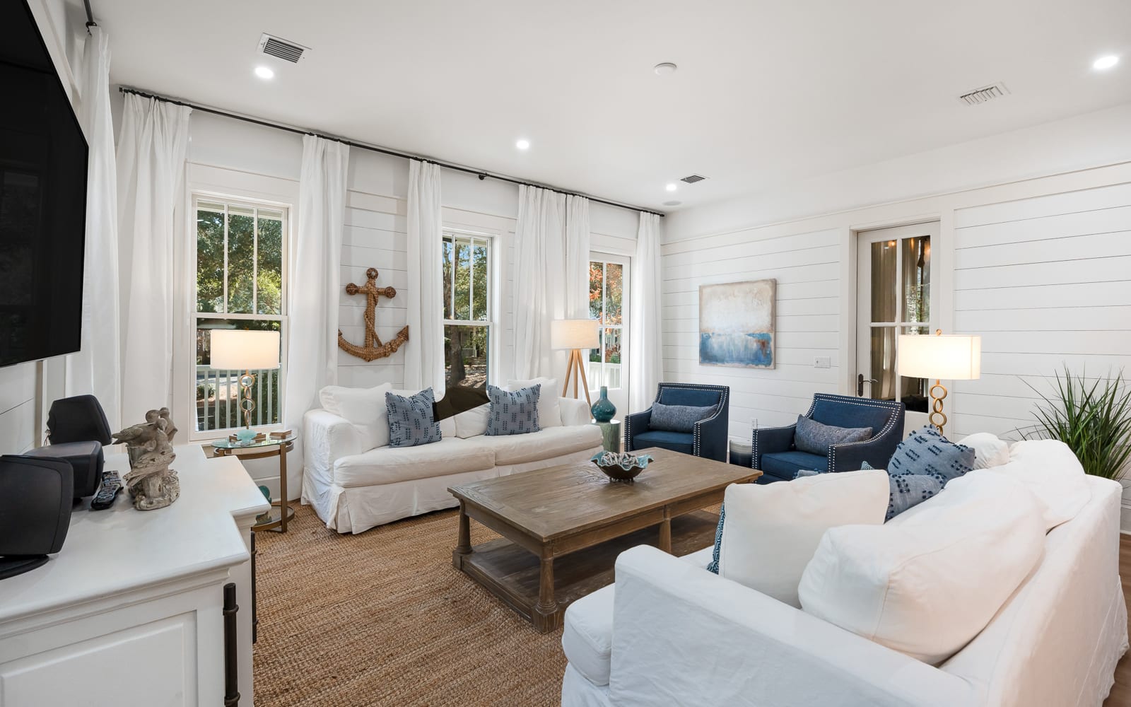 Relax in this coastal-inspired living room with nautical touches, crisp white shiplap walls, and plenty of natural light for your perfect getaway.