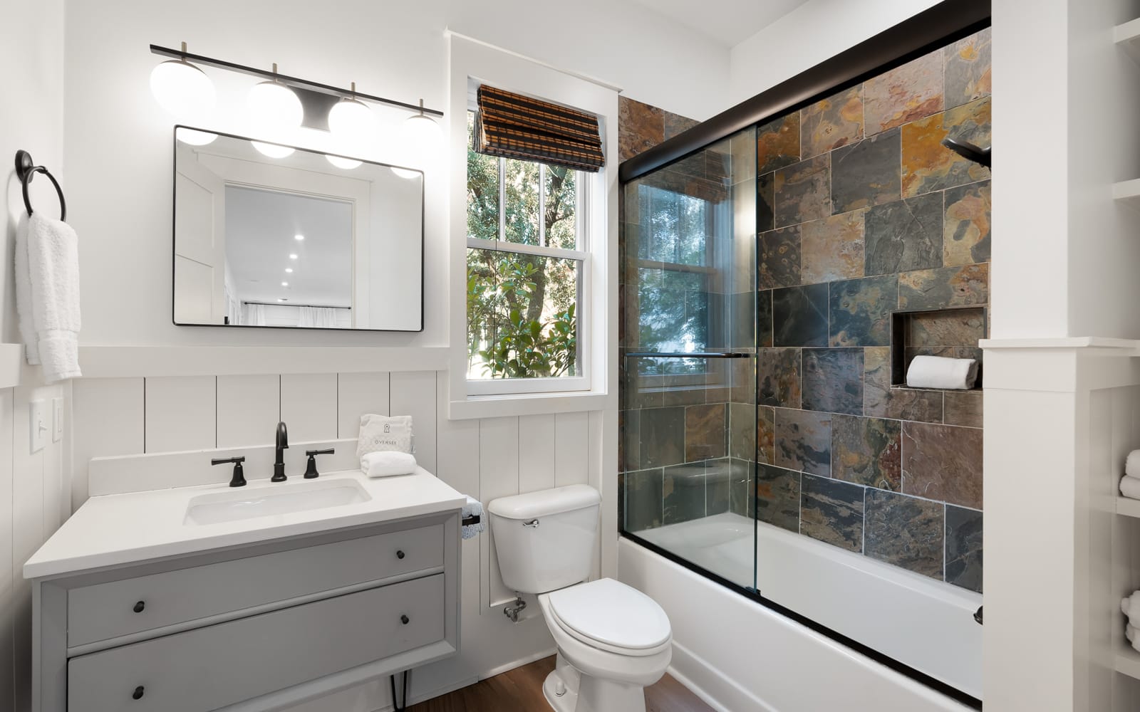 Unwind in your elegantly designed bathroom with stunning slate tile shower, modern fixtures, and peaceful garden views through charming windows.