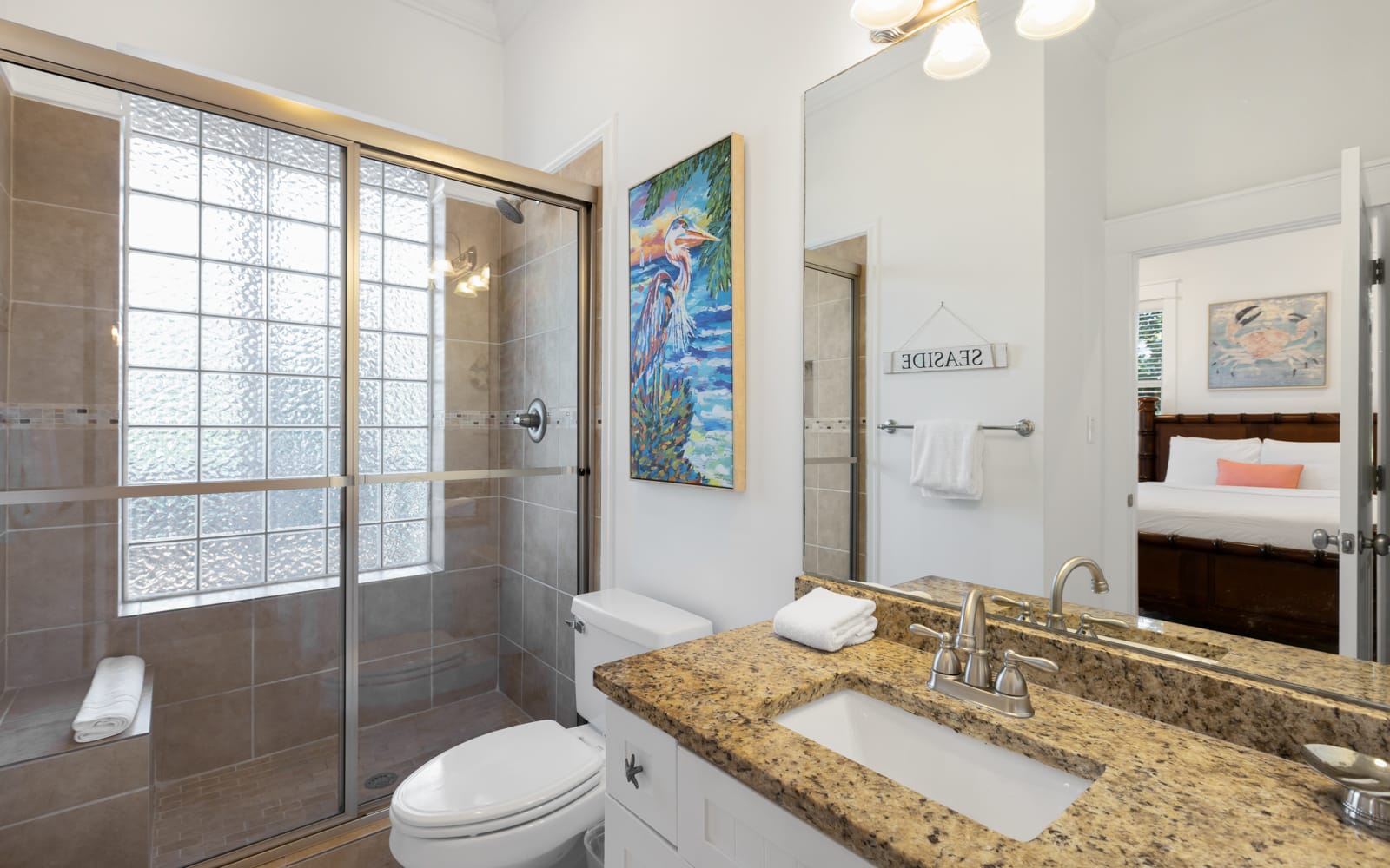 Your private bathroom features a spacious glass shower, granite countertops, and bright coastal artwork that adds charm to your daily routine.