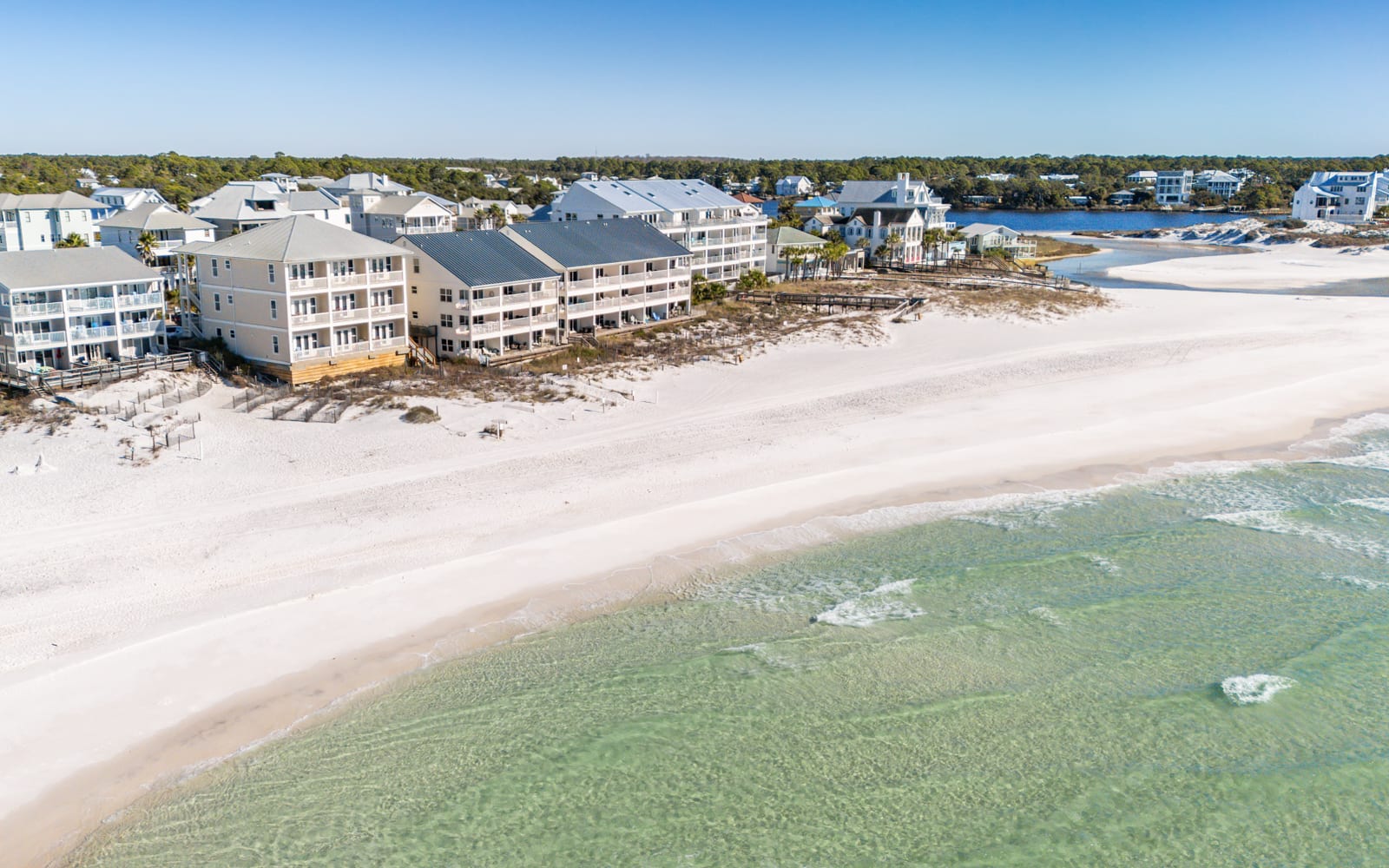 Aerial view of beachfront vacation rental properties situated directly on pristine white sand beach with crystal-clear emerald waters.