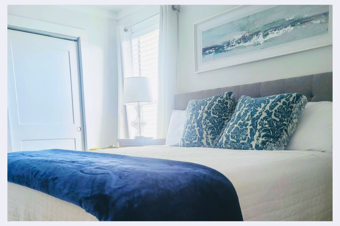 Drift off to sleep surrounded by soothing coastal blues and crisp white linens, where ocean-inspired artwork sets the perfect serene mood.