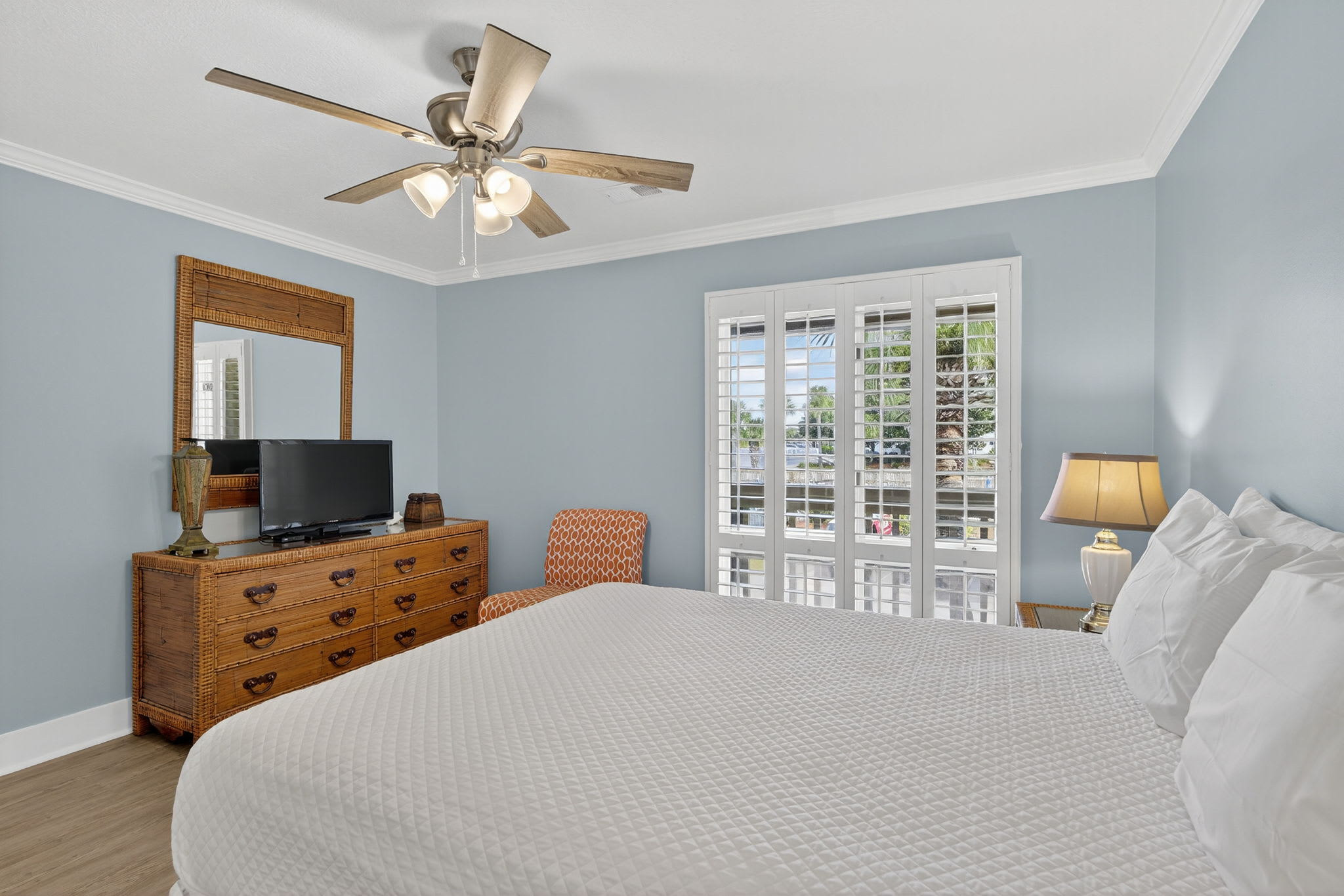 Relax in your serene bedroom featuring soothing blue walls, a comfortable bed with crisp linens, and French doors opening to your private balcony with outdoor views.