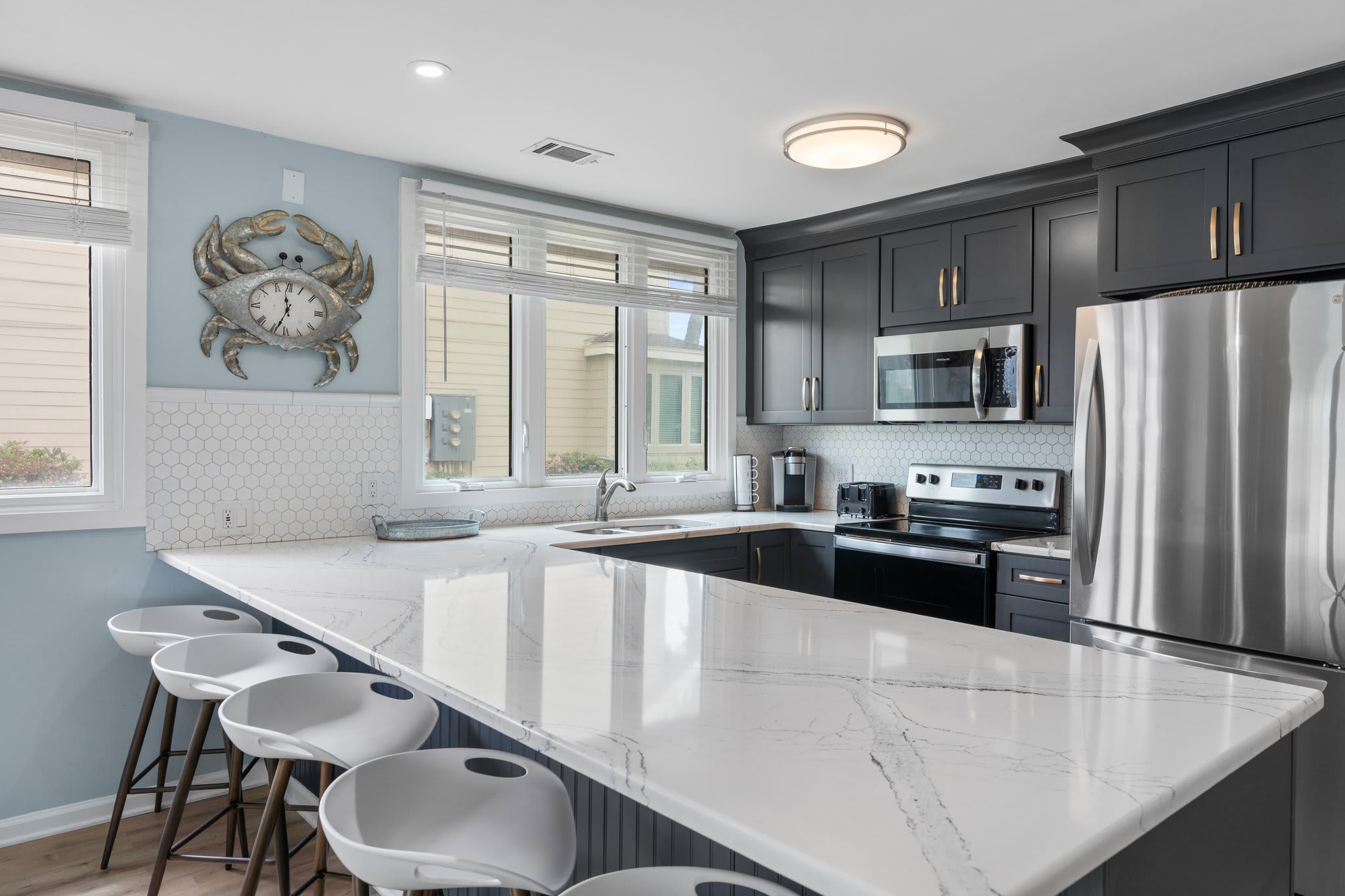 Modern kitchen with sleek dark cabinets, stainless steel appliances, and a large marble island with barstool seating for five—perfect for cooking, dining, and gathering with family and friends.