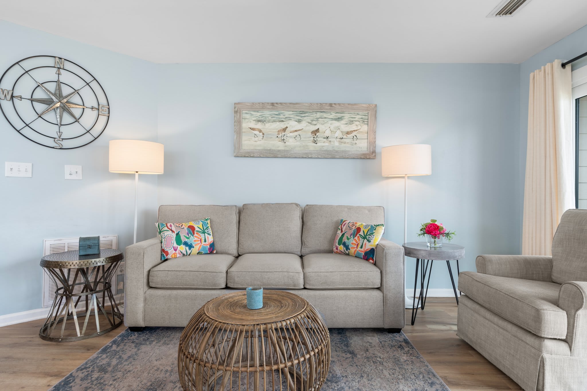 Charming coastal living room with a comfy sofa, beachy artwork, rattan coffee table, and soft blue walls—perfect for unwinding after a sunny day at the beach.