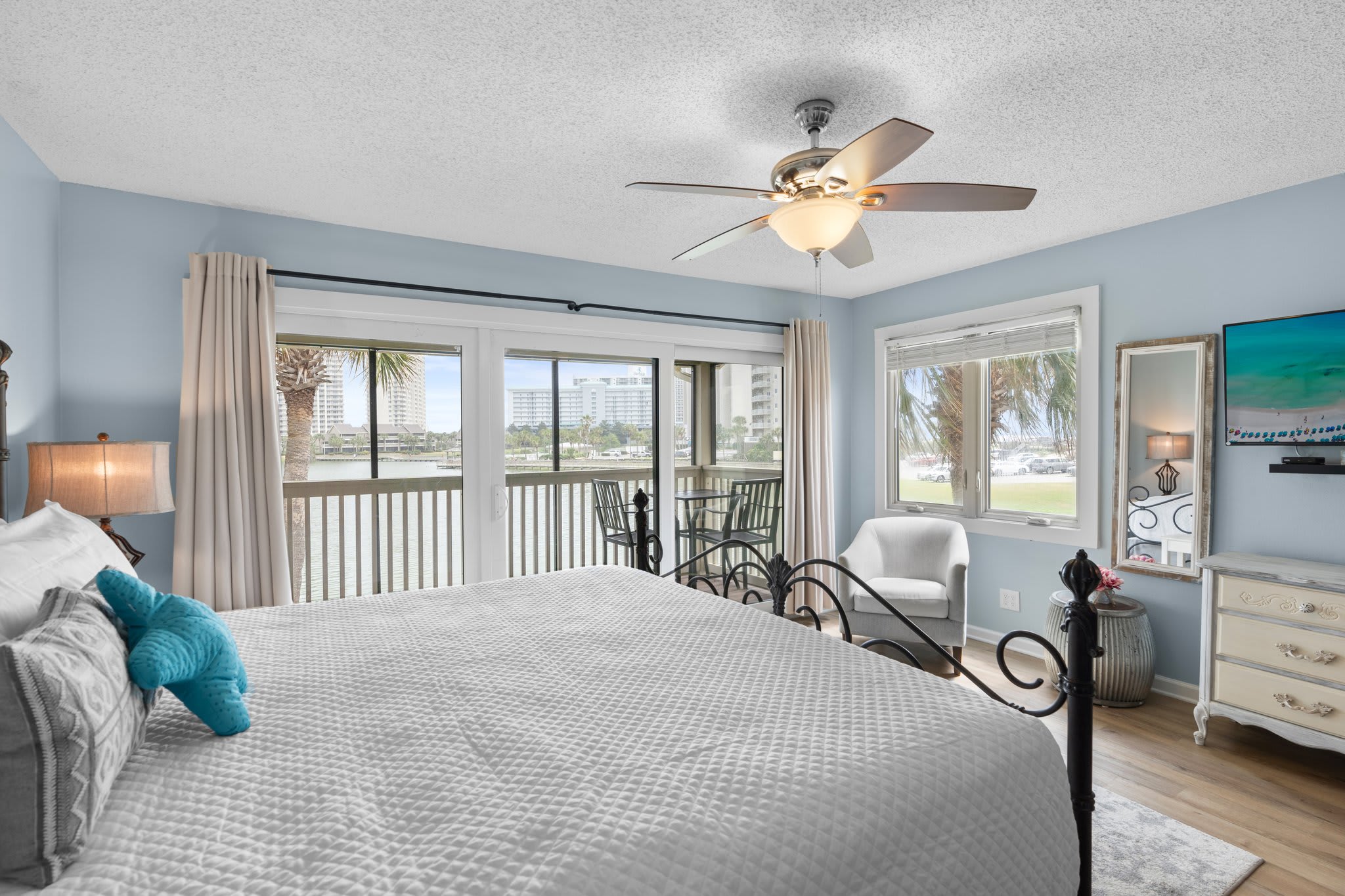 The primary bedroom boasts panoramic lake views, a king bed, cozy reading chair, and private balcony access—offering a peaceful and scenic coastal escape.