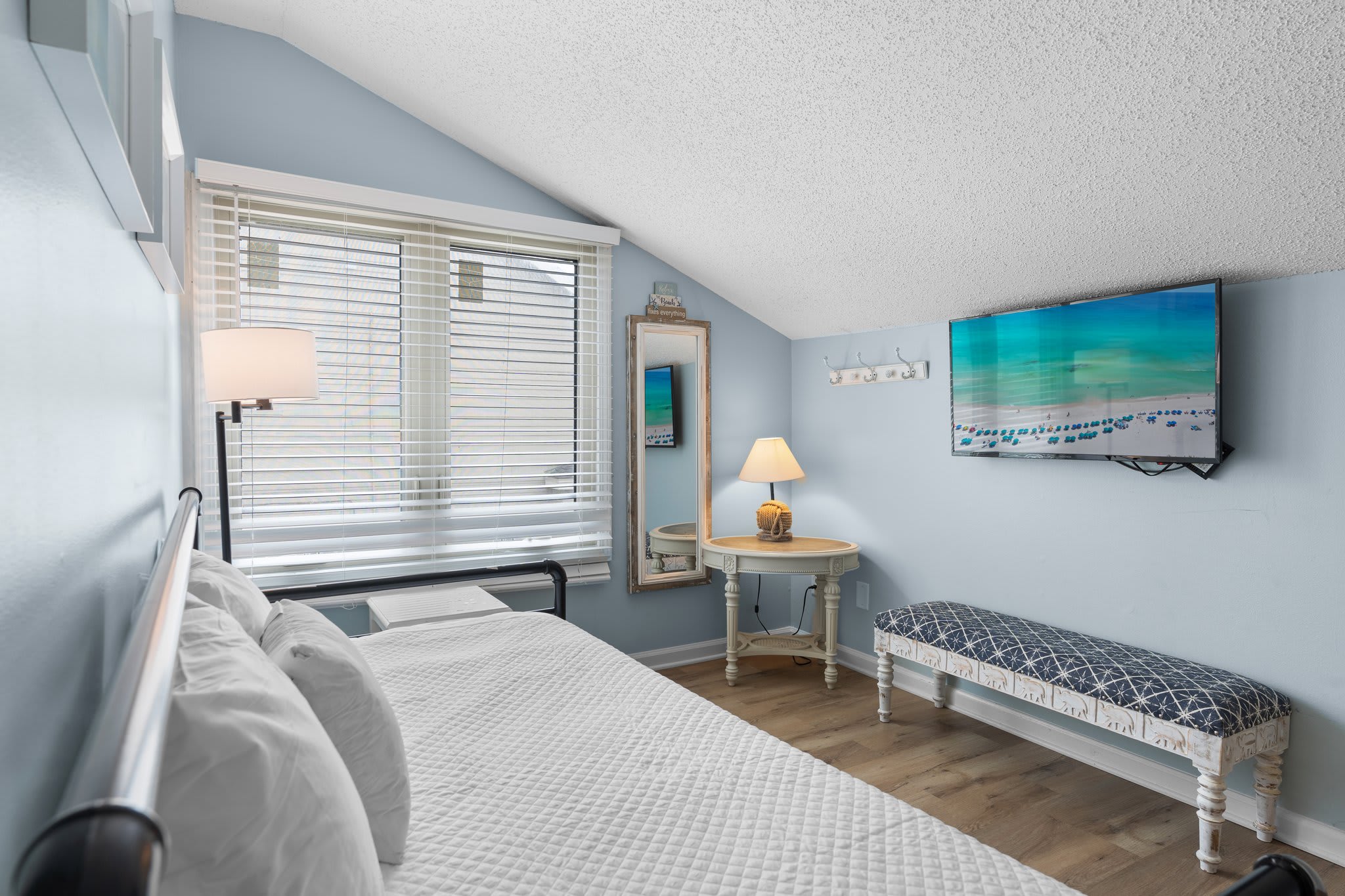 Bright and airy guest loft with a convertible daybed, wall-mounted TV, reading nook, and coastal décor—offering comfort and flexibility in a tranquil upstairs retreat.