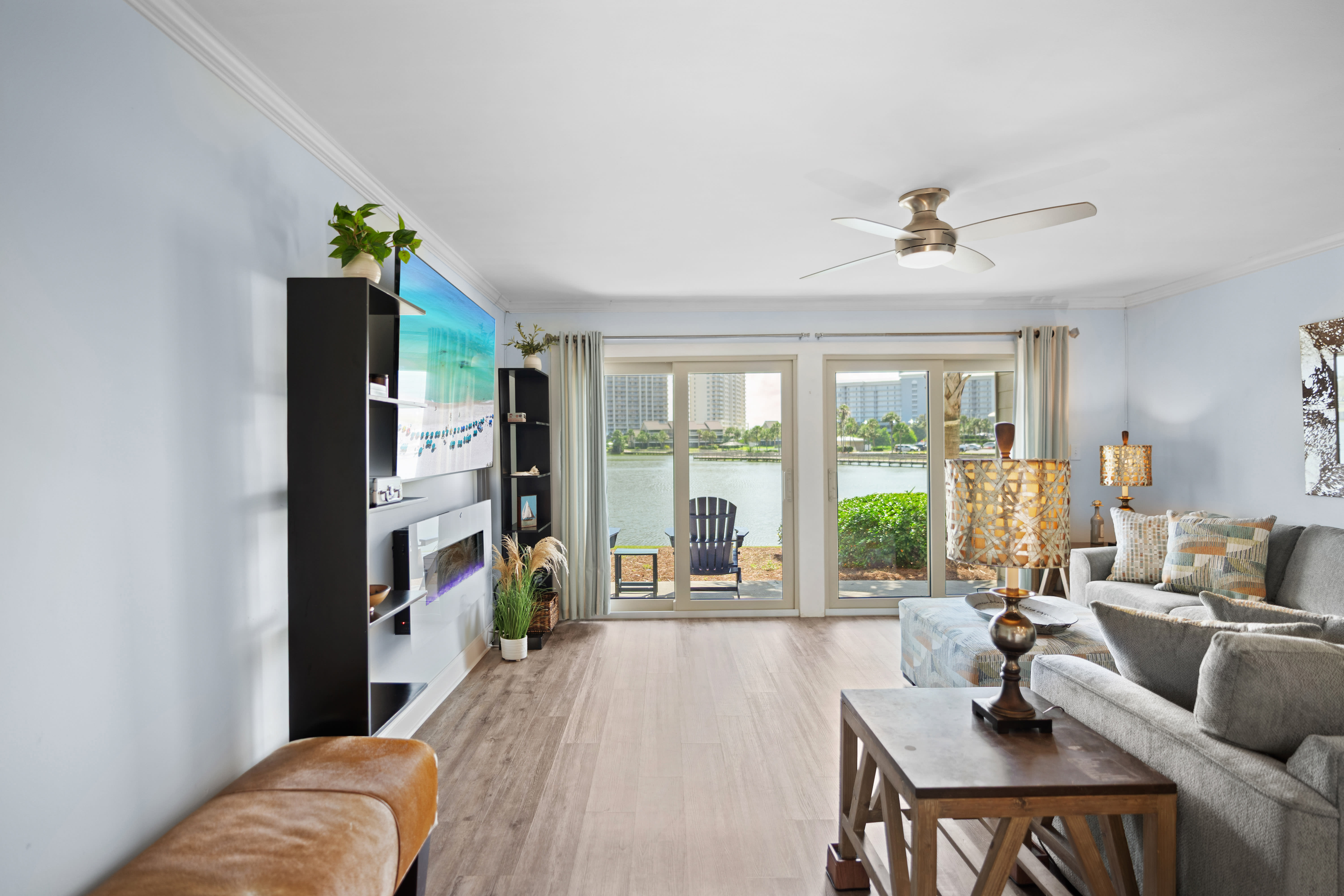 Spacious lakefront living room with modern decor, large glass doors, electric fireplace, and LVP wood floors. Features patio access and stunning water views.